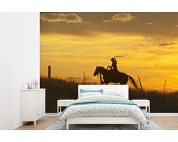 Behang - Fotobehang Een cowboy onder een oranje hemel - Breedte 305 cm x hoogte 220 cm
