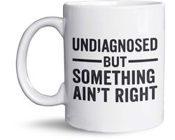 NietMokken.nl - Mok – UNDIAGNOSED BUT SOMETHING AIN’T RIGHT – Grappige mok met tekst – Cadeau voor sarcastische types – Koffiemok 325ml – Keramiek – Aan beide zijden bedrukt – Voor werk en thuis - Voor collega